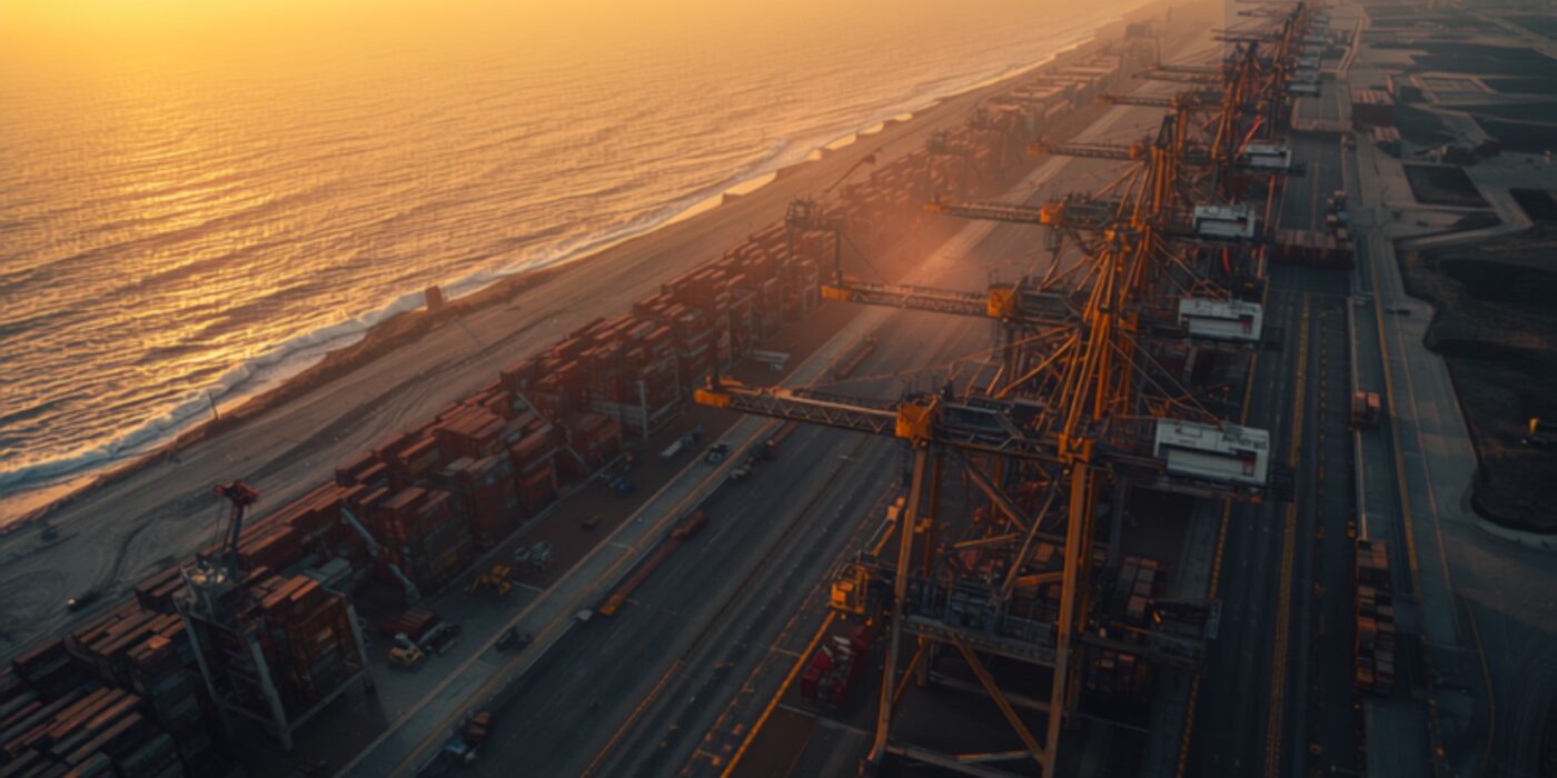Aerial view of a large container port at sunrise with rows of cargo cranes and stacked shipping containers along a coastline