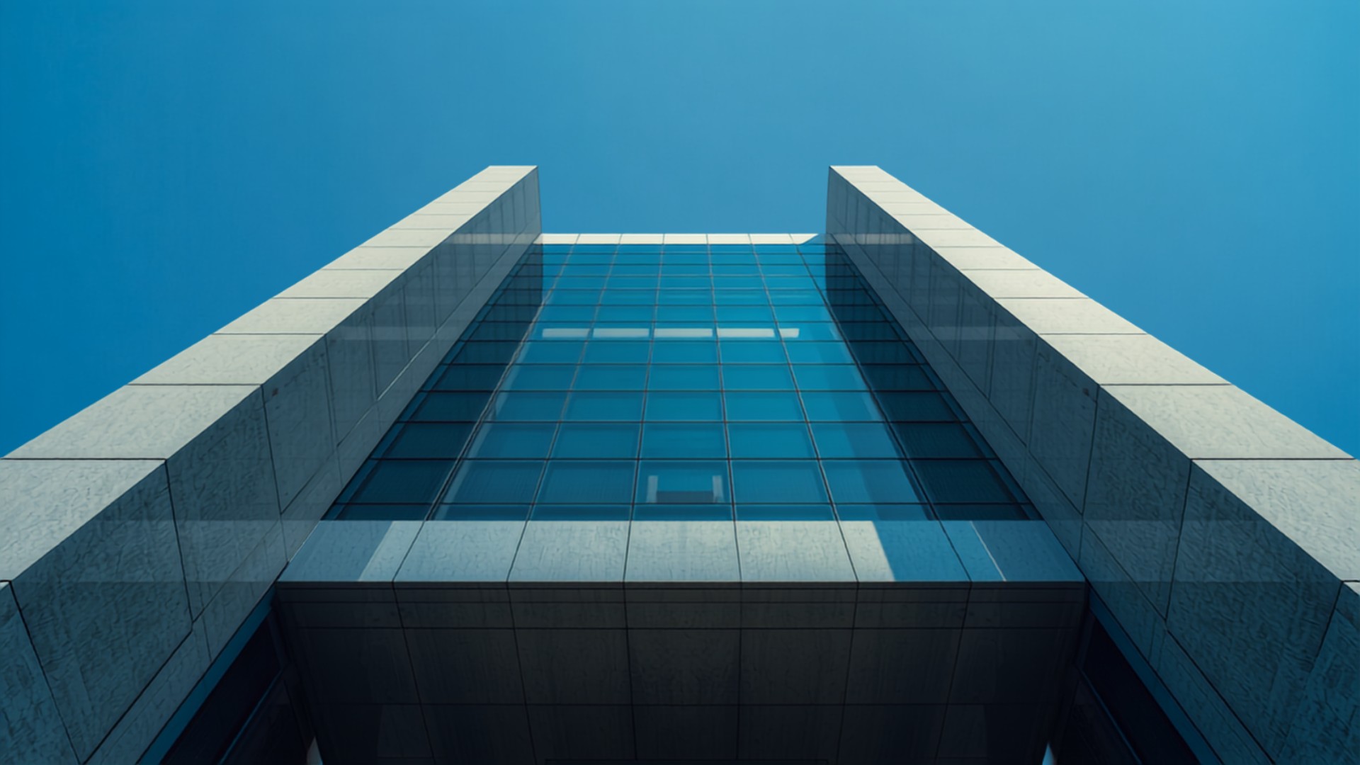 Upward view of a modern glass and stone office building against a clear blue sky