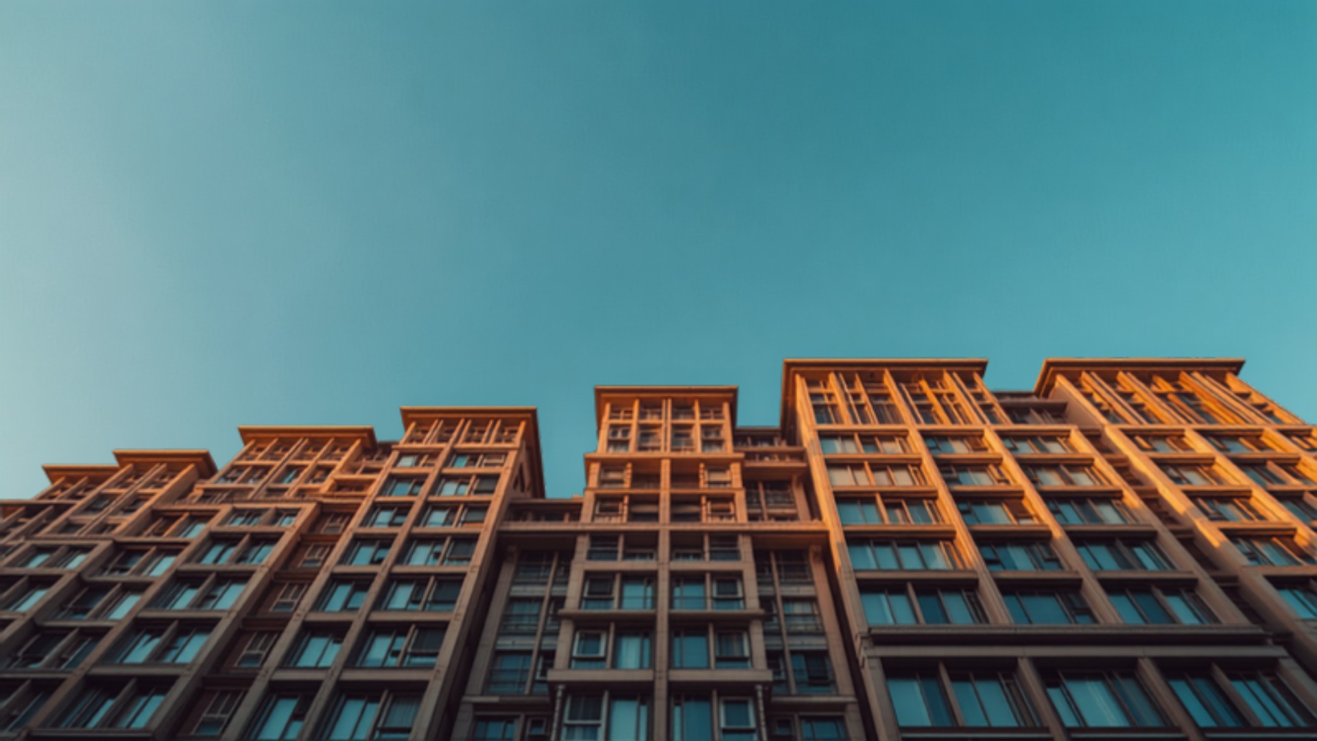 Low-angle view of a multi-story brick apartment building against a clear blue sky, highlighting its grid of windows.