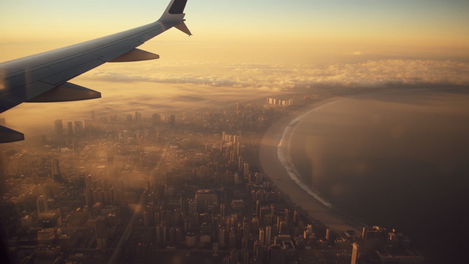 Aerial view of an Indian coastal city skyline and shoreline seen from a plane window at golden hour
